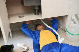 Rhino Rooter plumber fixing pipes under a sink, showing readiness to handle any sewer or drain cleaning problem.