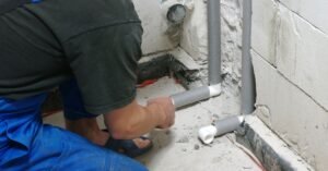 Rhino Rooter team member adds insulation foam to pipes in a room being fixed up.